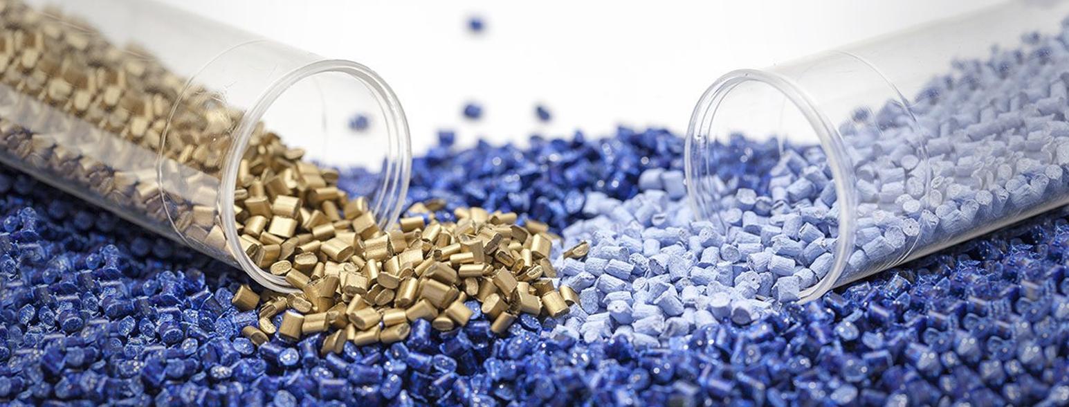 Zwei Glastuben sind mit Plastik Granulat in gold oder hellblau gefüllt. Sie liegen auf dunkelblauem Granulat.